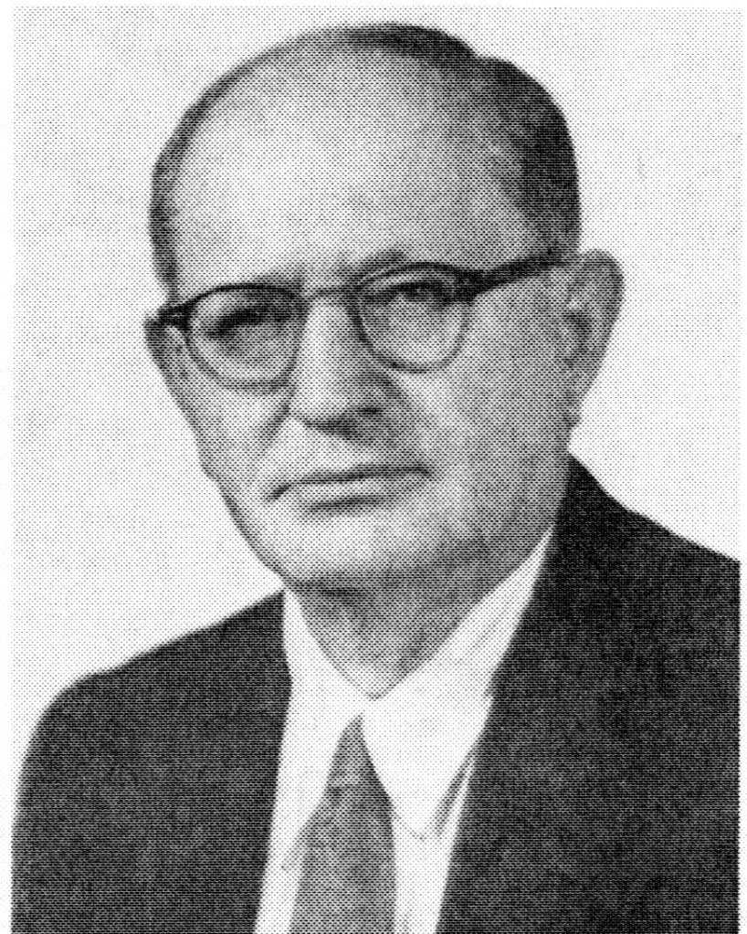 Black and white portrait of a middle-aged man with glasses, wearing a suit and tie, looking directly at the camera.