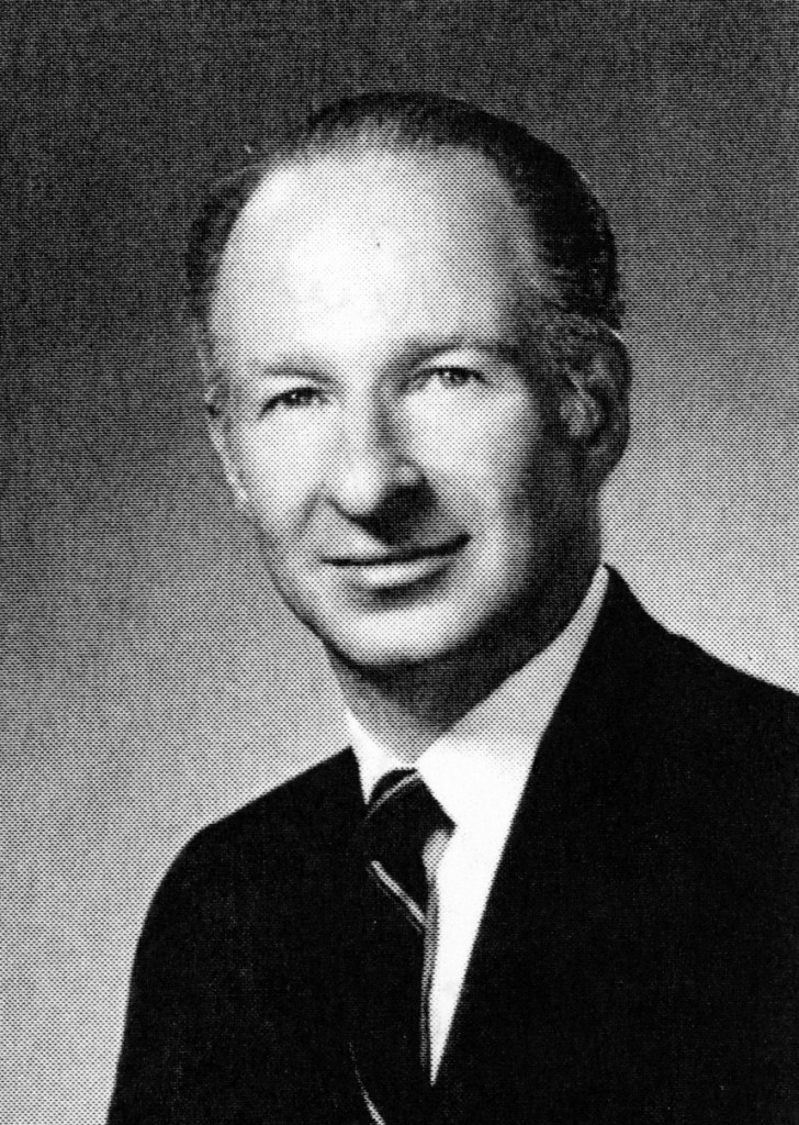 Black and white portrait of a middle-aged man in a suit and tie, smiling at the camera.