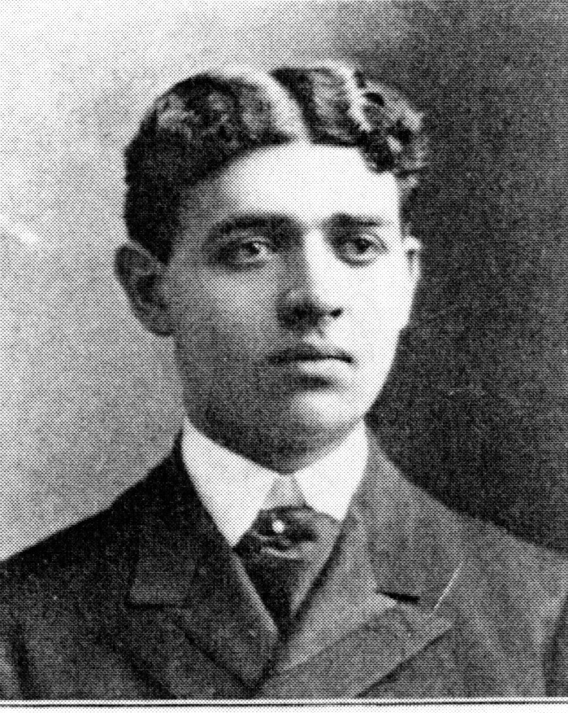 A black and white portrait of a young man with neatly styled hair, wearing a formal suit and tie.