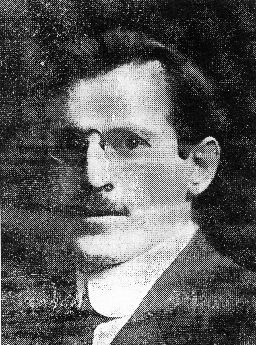A vintage black and white portrait of a man with glasses and a mustache, dressed in a suit and tie, looking directly at the camera.