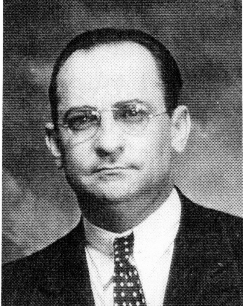 A black and white portrait of a man wearing glasses and a suit, with a serious expression.