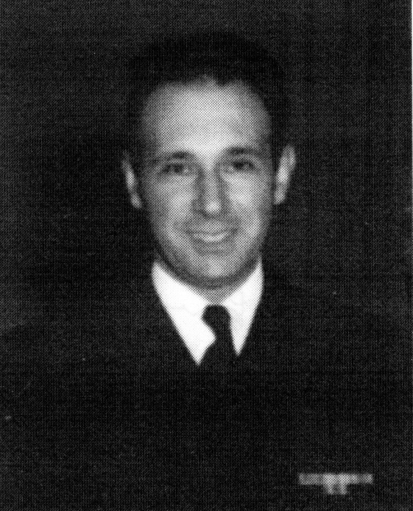 Black and white portrait of a smiling man in a suit and tie, with a light-colored shirt and a dark background.