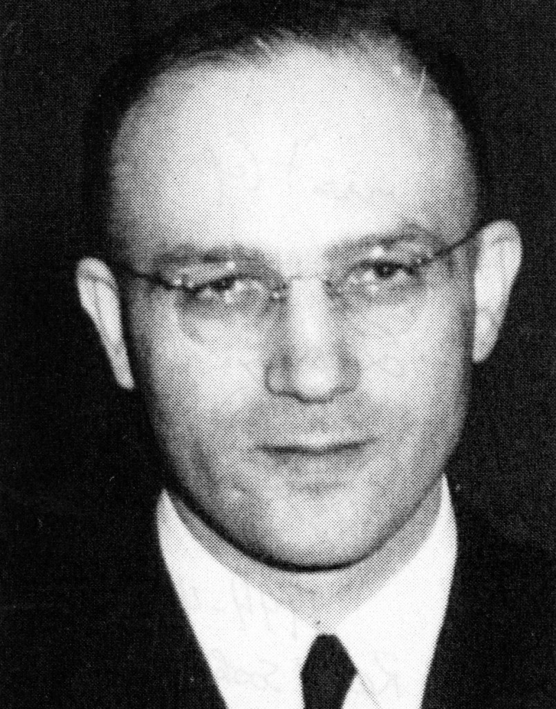 Black and white portrait of a man wearing glasses and a suit, with a neutral expression.