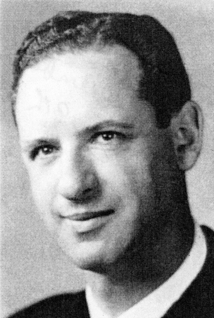 Black and white portrait of a man with short hair, wearing a suit and tie, smiling softly.